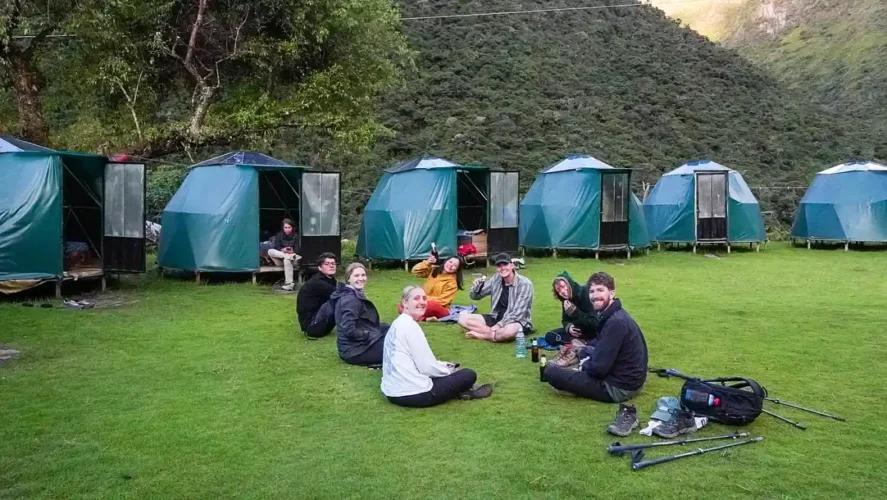 Group of trekkers resting on the grass at camp during the third day of the Salkantay Trek, enjoying the peaceful Andean landscape and preparing for the next leg of their journey.